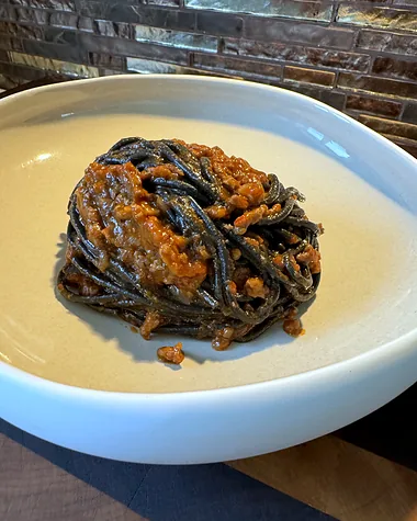 A nest of black squid ink pasta with shellfish, in a shallow white bowl