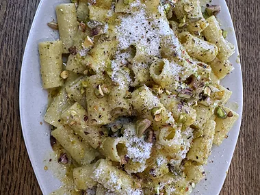 A large oval platter of rigatoni with grated cheese and chopped nuts, on a wooden table