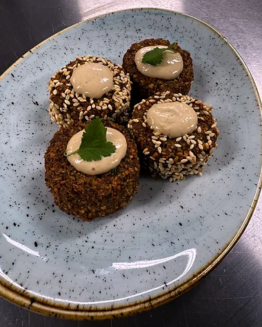 Four sesame-crusted stuffed dates topped with soft cheese, on a speckled teal plate
