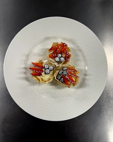 A small tartlet plated in the centre of a wide white plate, dressed with herbs