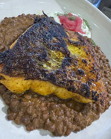 A charred salmon fillet on spiced lentils, with pickled red onion and a dill yoghurt